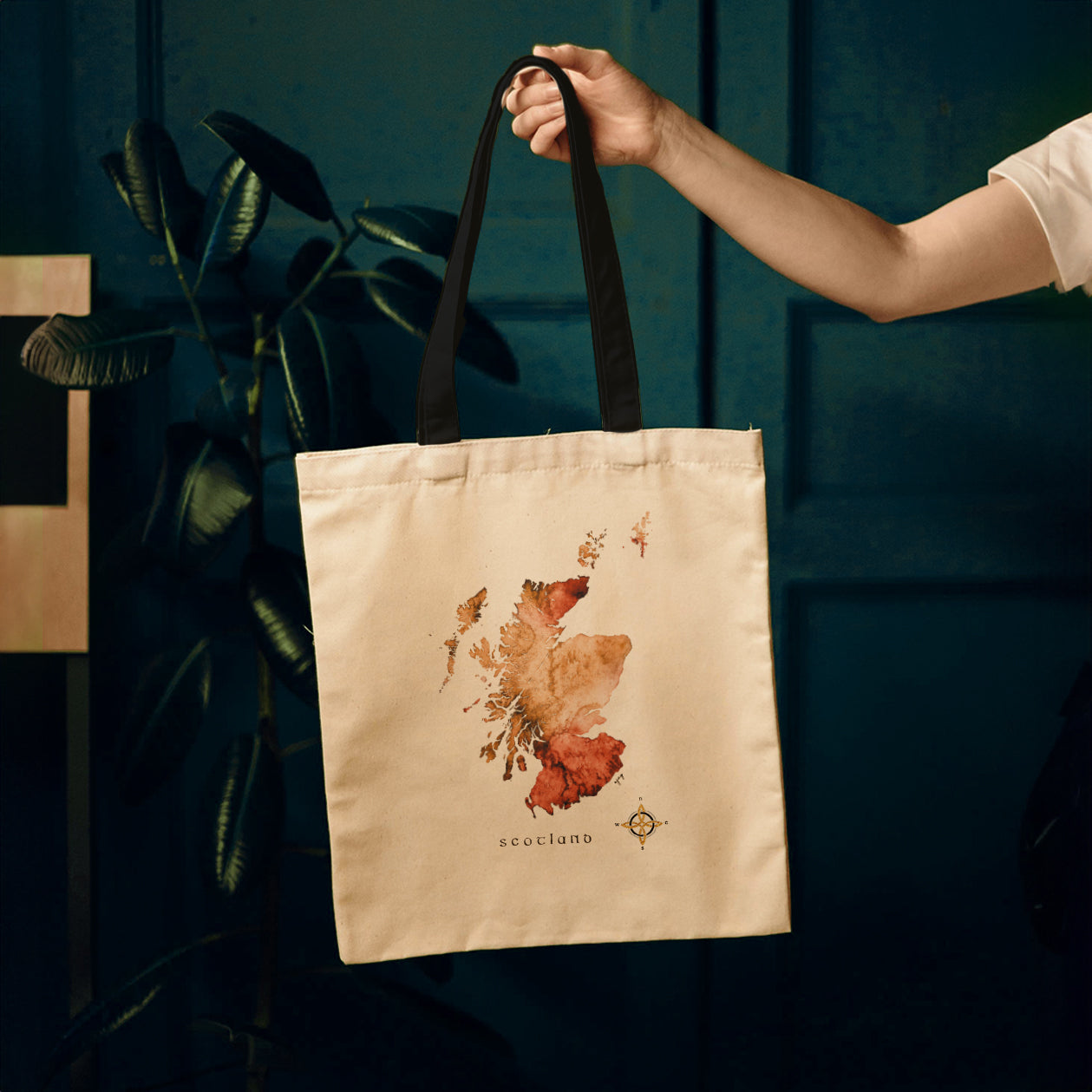 Hand holding a tote bag featuring a vibrant watercolour map of Scotland.