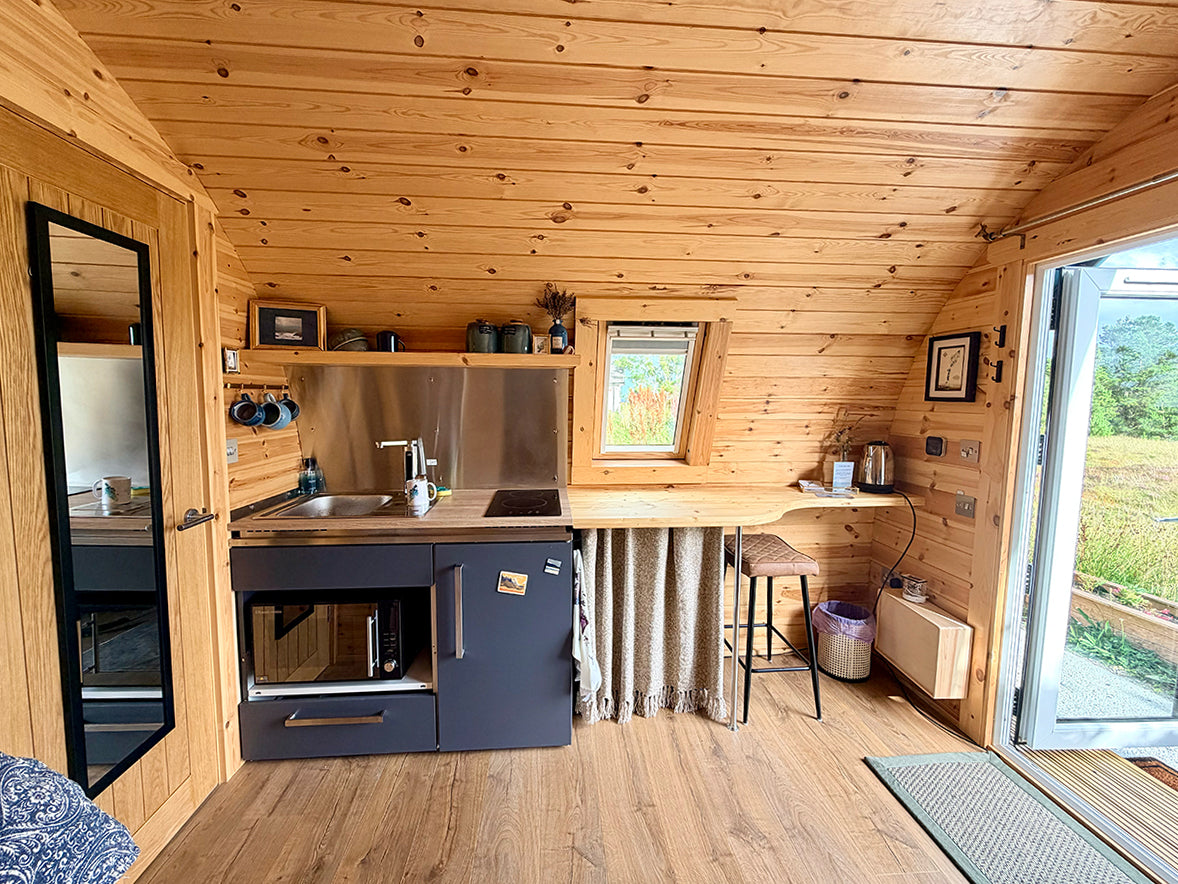 A compact kitchenette inside a log cabin pod  with light wood paneled walls and ceiling, a dark gray cabinet base, stainless steel sink and backsplash, by ejaydesign