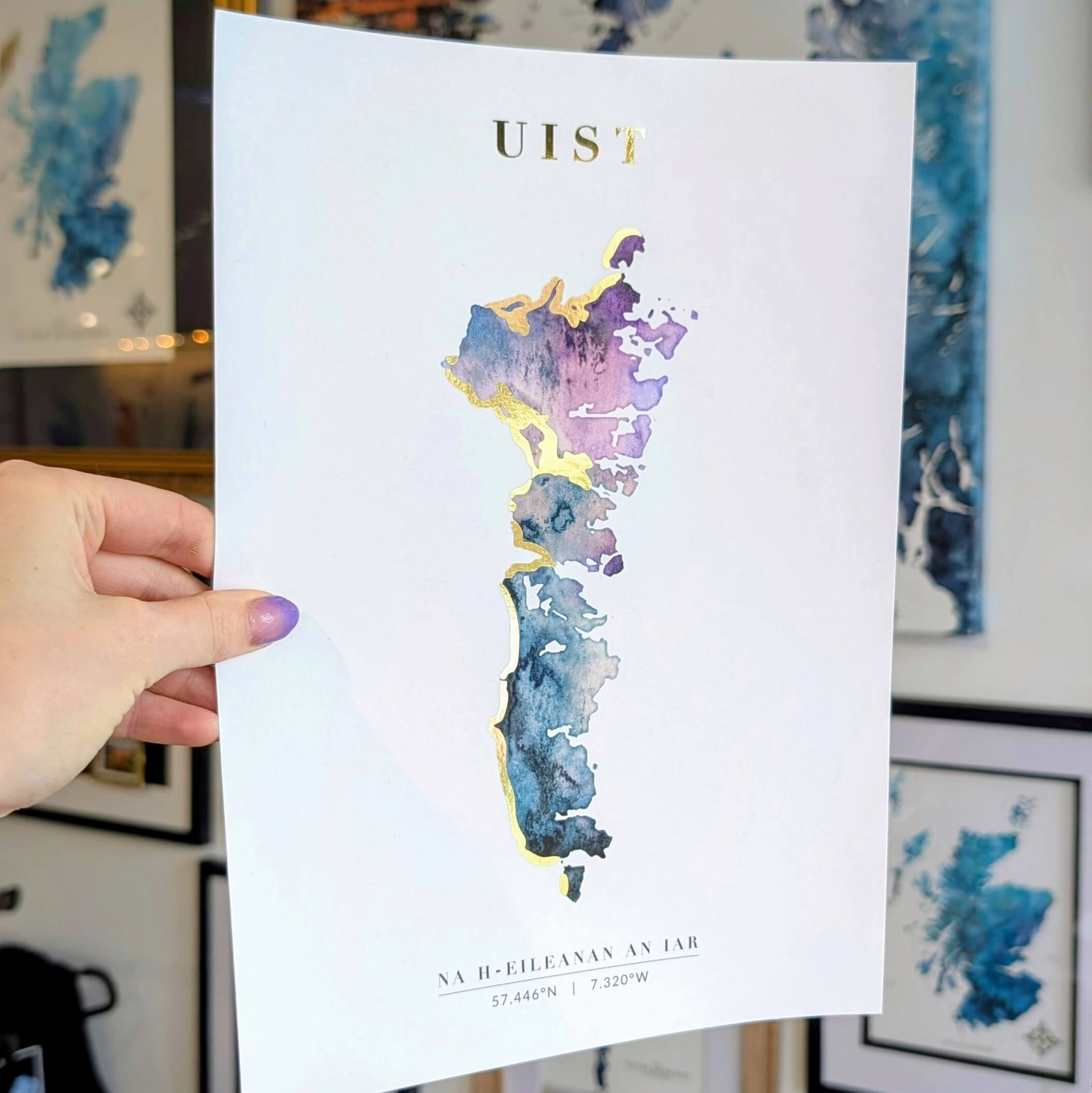 Hand holding a watercolour map print of Uist with gold highlights outlining the island’s beaches